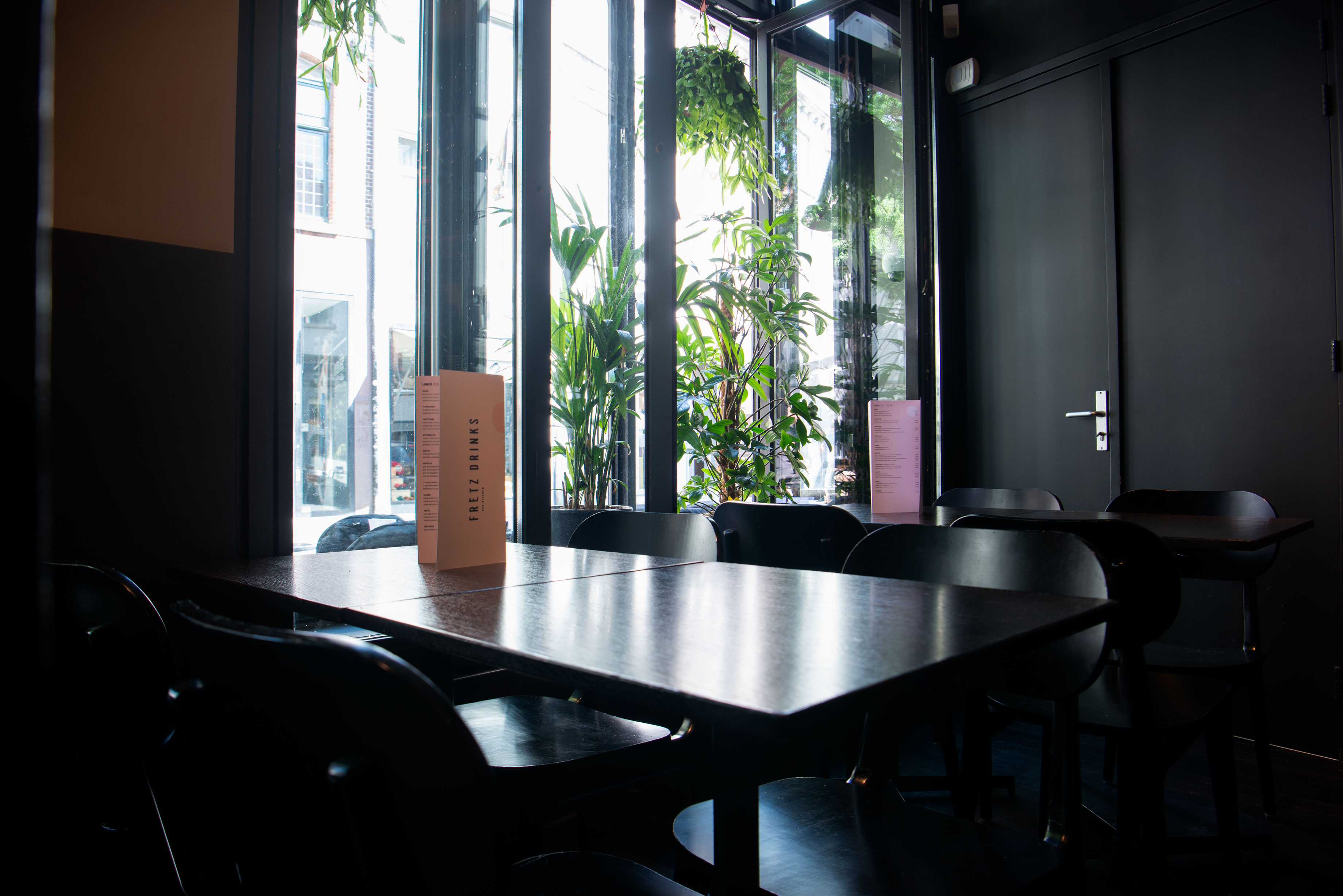 Tables and chairs at the window with plants. There are menus on the tables.